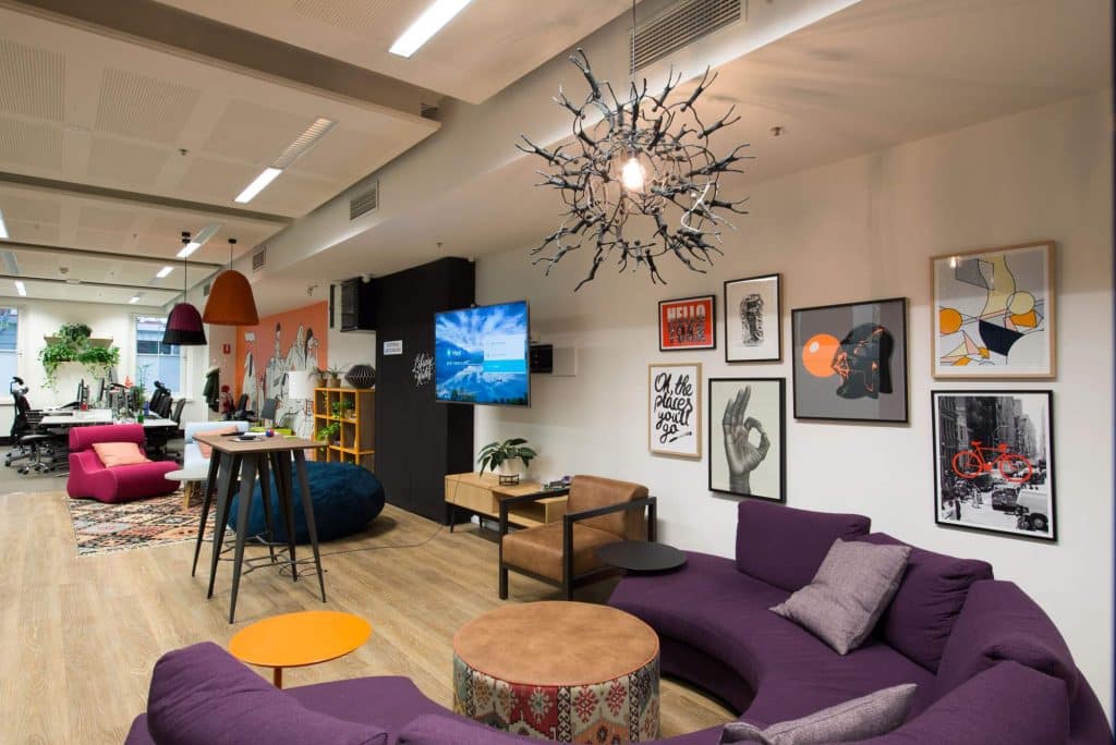 polished floor boards, casual circular couch, wall art, funky lighting tv screen and table as an interior design area for employees to relax in their workspace