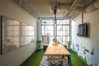 Narrow office area with white walls, long wooden bench, whiteboard, tv