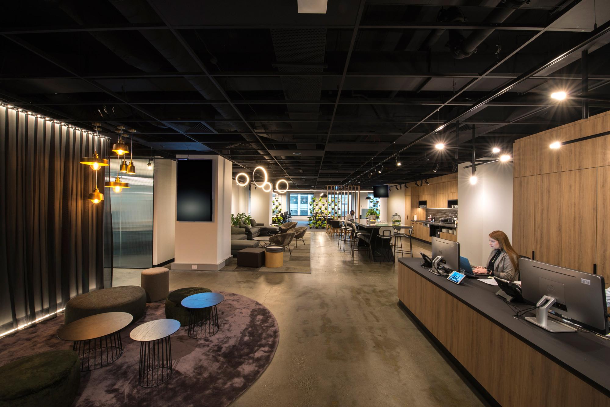 Business reception on right with casual waiting area opposite with stools on rug and kitchen in background