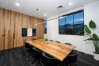 Meeting room, wooden table, black chairs, windows in background, black carpet.