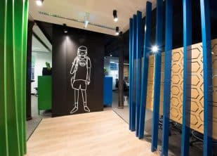 Best office interior design using green vertical panels on left and blue ones on right as entry to office with black wall and white figurine with entry to office going left or right. Light sand floor boards and downlights to highlight entry to office