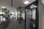 Office fitout. Modern private meeting pods on right with glass walls, walk through in middle with grey carpet, planters on left to divide workspace. Modern downlights and interior fittings