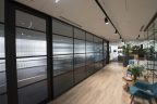 New modern office fitout. Light floorboards at entrance, glass walls with black frame squares, modern down lights, lots of plants, white ceilings.