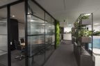 New office design. Grey carpet, meeting room on left with glass that has privacy film, opposite are planter boxes with plants to divide workspace and modern interior fittings put in place.